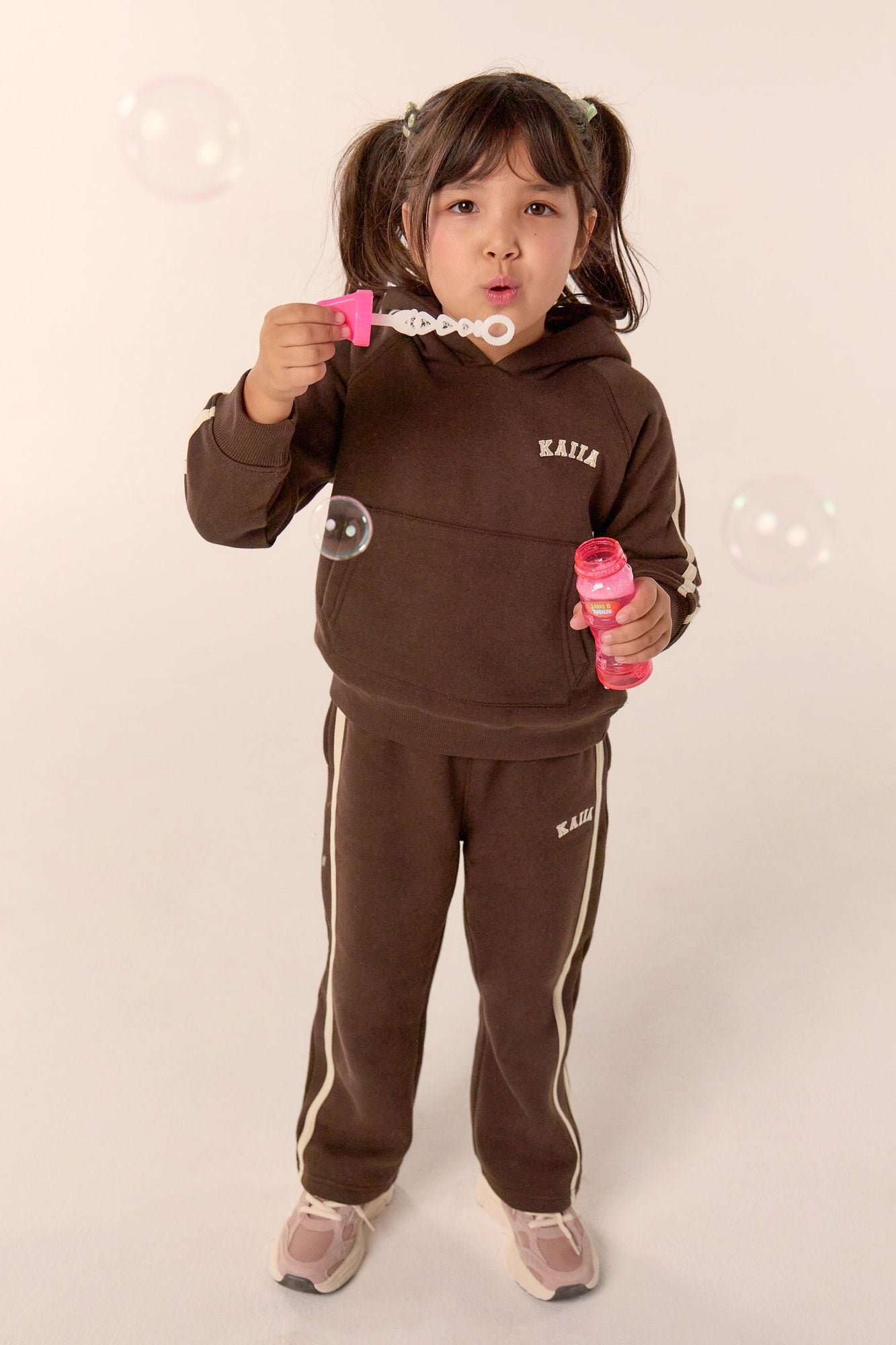 Child in brown hoodie and joggers blowing bubbles while holding bubble wand
