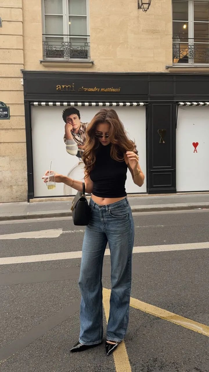 Vrouw in zwart crop top en wijde jeans poseert voor luxe winkelfront op straat