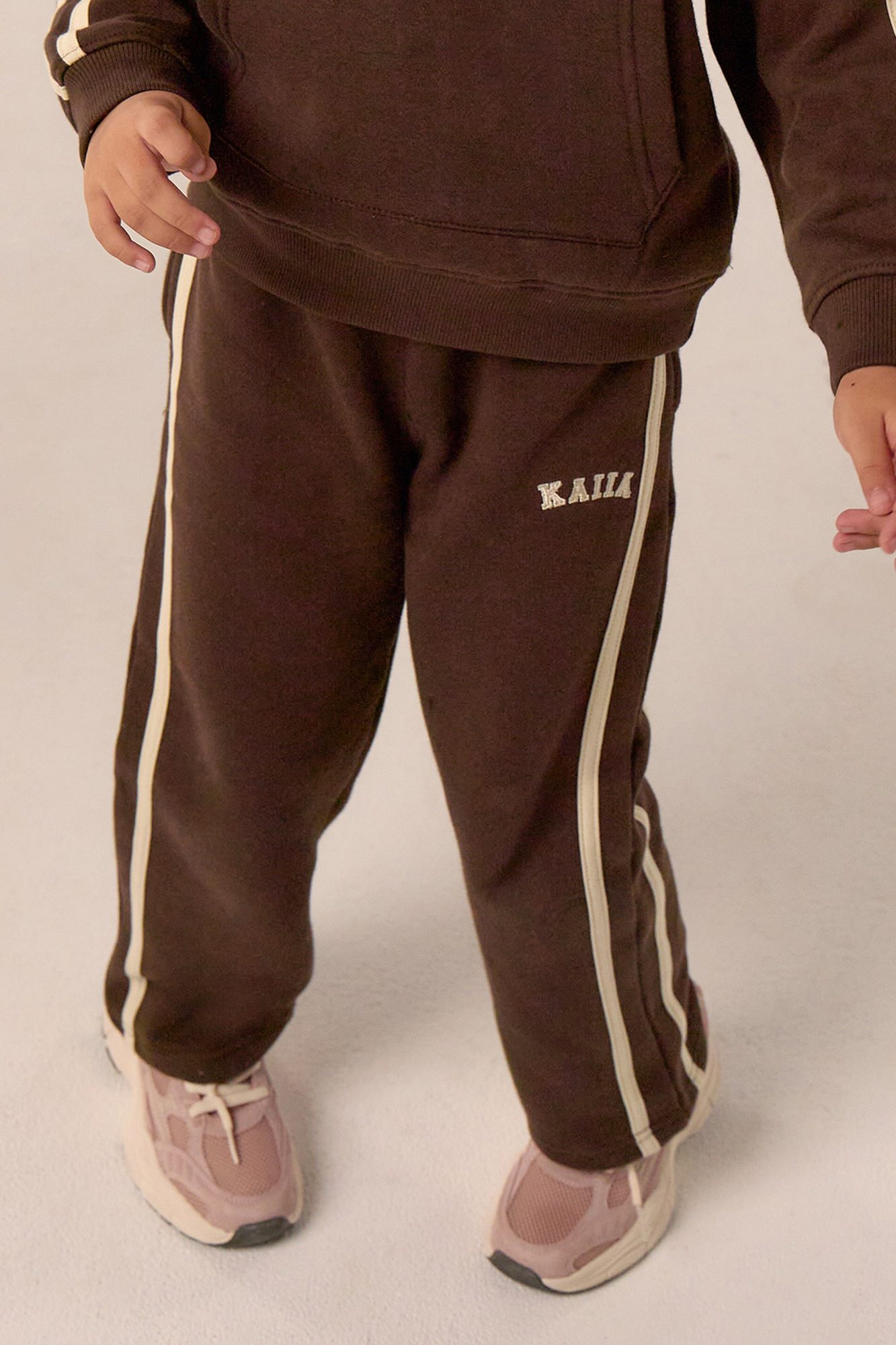 Close-up of child's legs wearing brown joggers with cream side stripes and pink sneakers