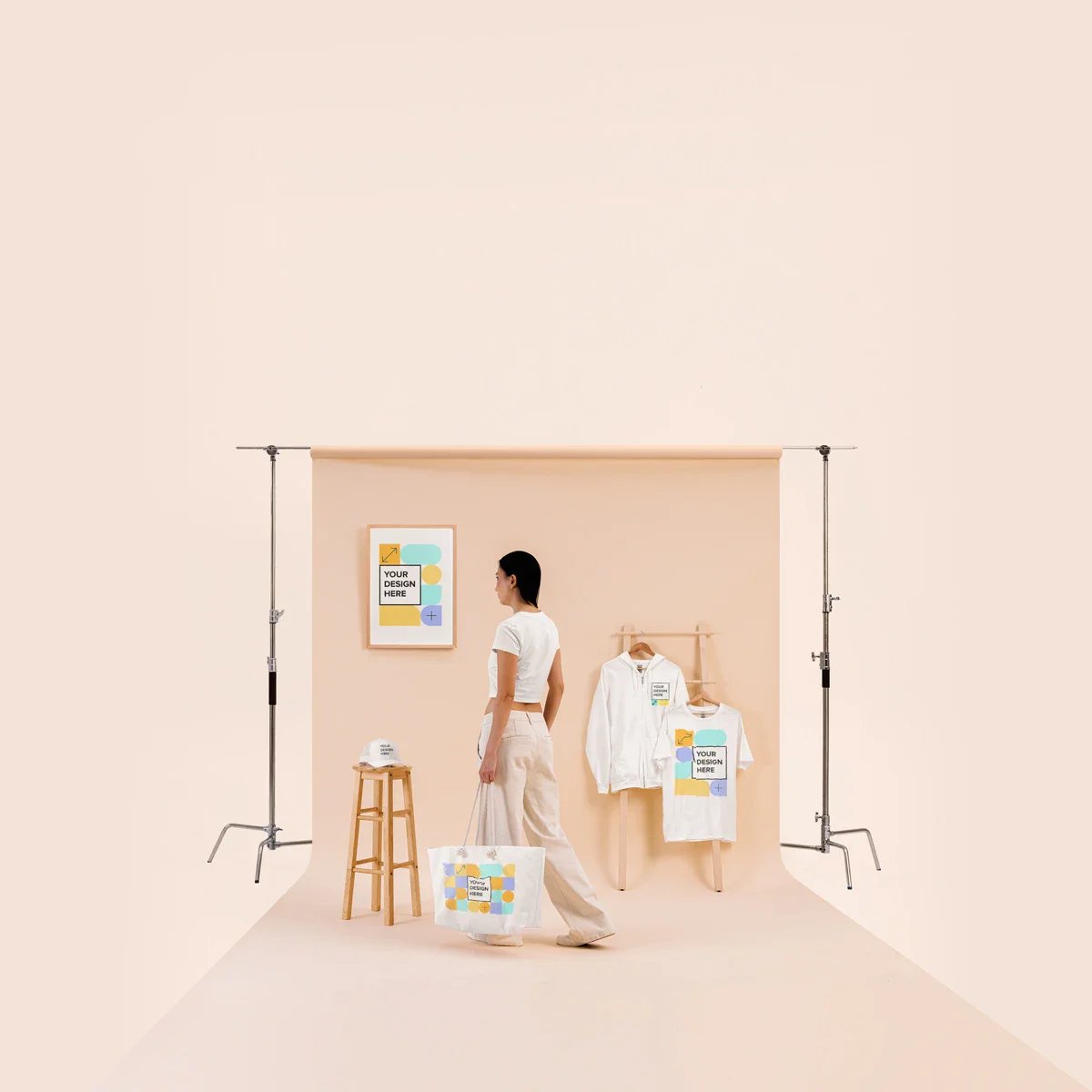 Mujer de perfil con prendas blancas estampadas cerca de bolsa, cartel decorativo y perchero de madera en estudio beige