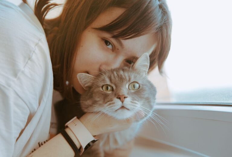 Woman holding and cuddling a gray tabby cat near a window